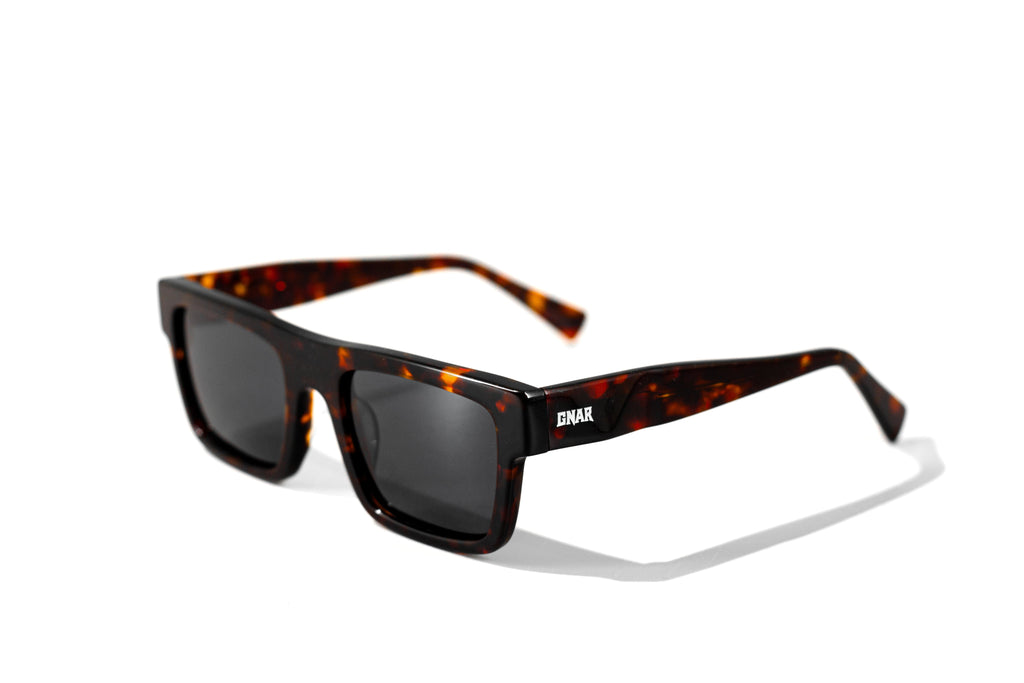 Front view of Gnar Optics Sender sunglasses with rectangular tortoise acetate frames, dark grey polarized lenses and a white GNAR logo on the arm