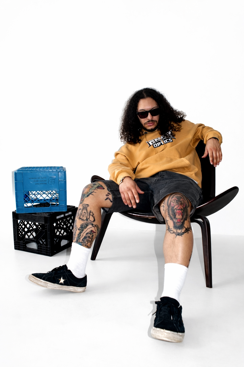 Tattooed man wearing GNAR Optics sender sunglasses and mustard hooded sweat top while seated in a chair